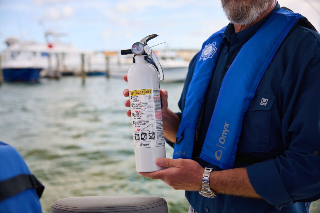 A man wearing a life jacket holding a boat fire extinguisher, safe boating concept.