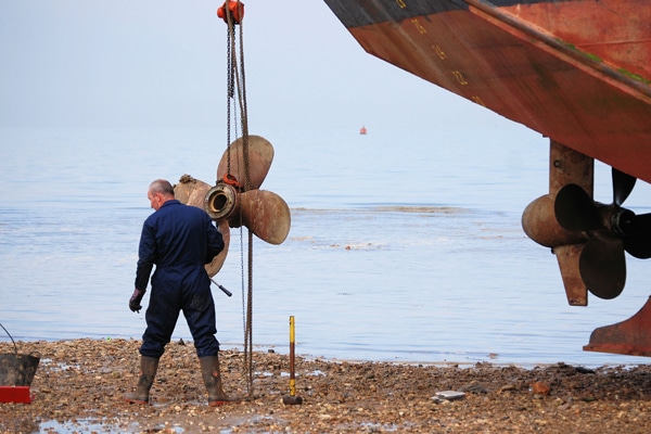 A man on shore conducting boat prop repair.