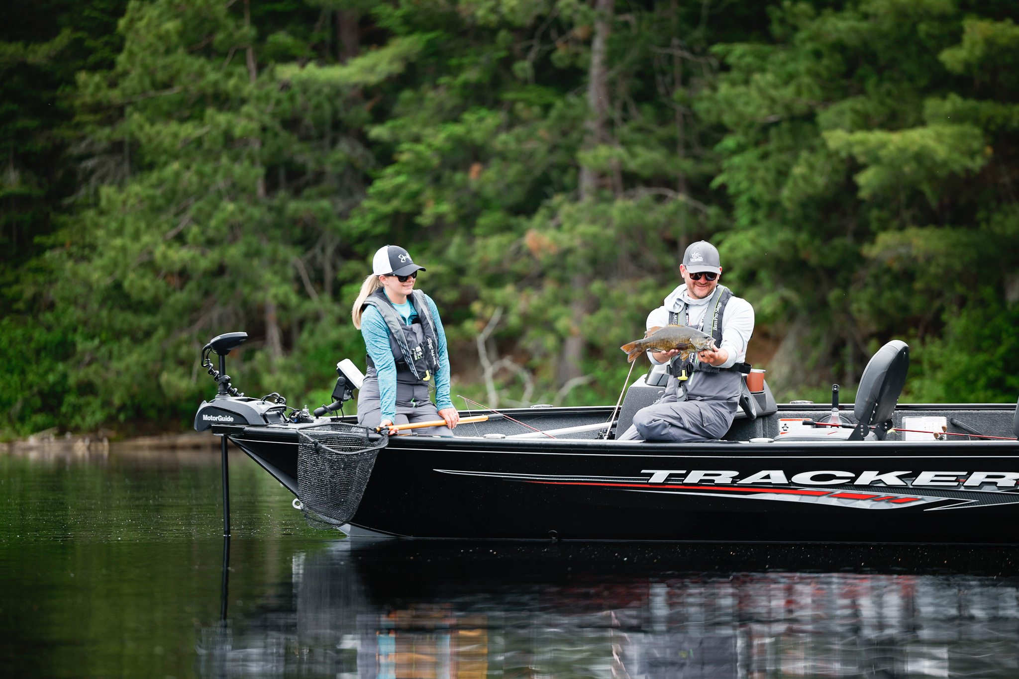 Two people fishing in a boat, one person holds a fish they caught, fishing and boating in Kentucky concept.