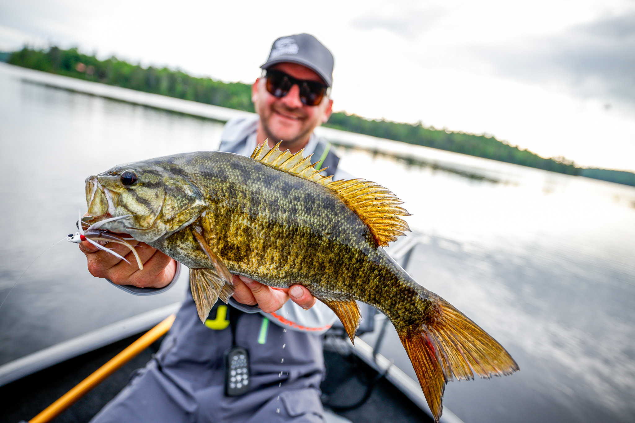 An angler on a lake in a boat holds up a fish.