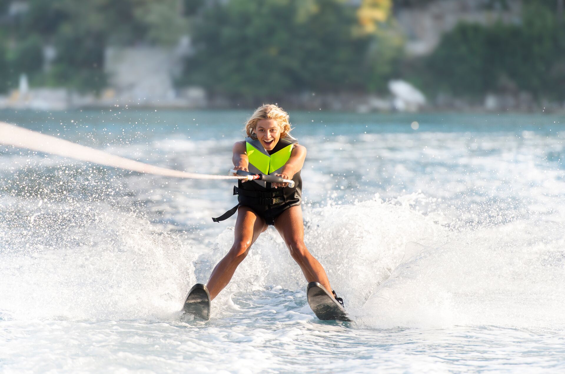 A girl water skiing while smiling and wearing a life jacket.