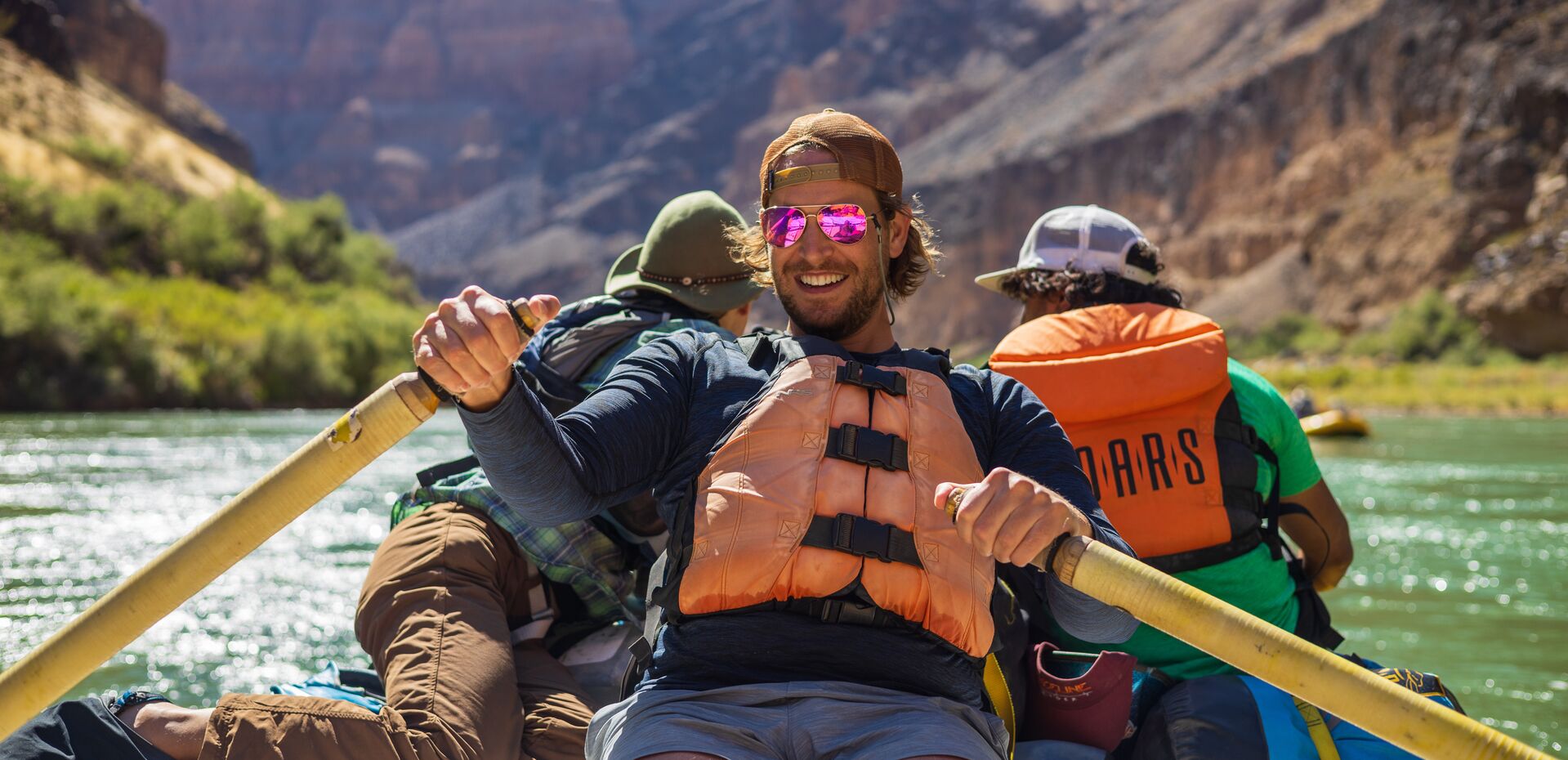 People smiling and wearing life jackets while whitewater rafting. 
