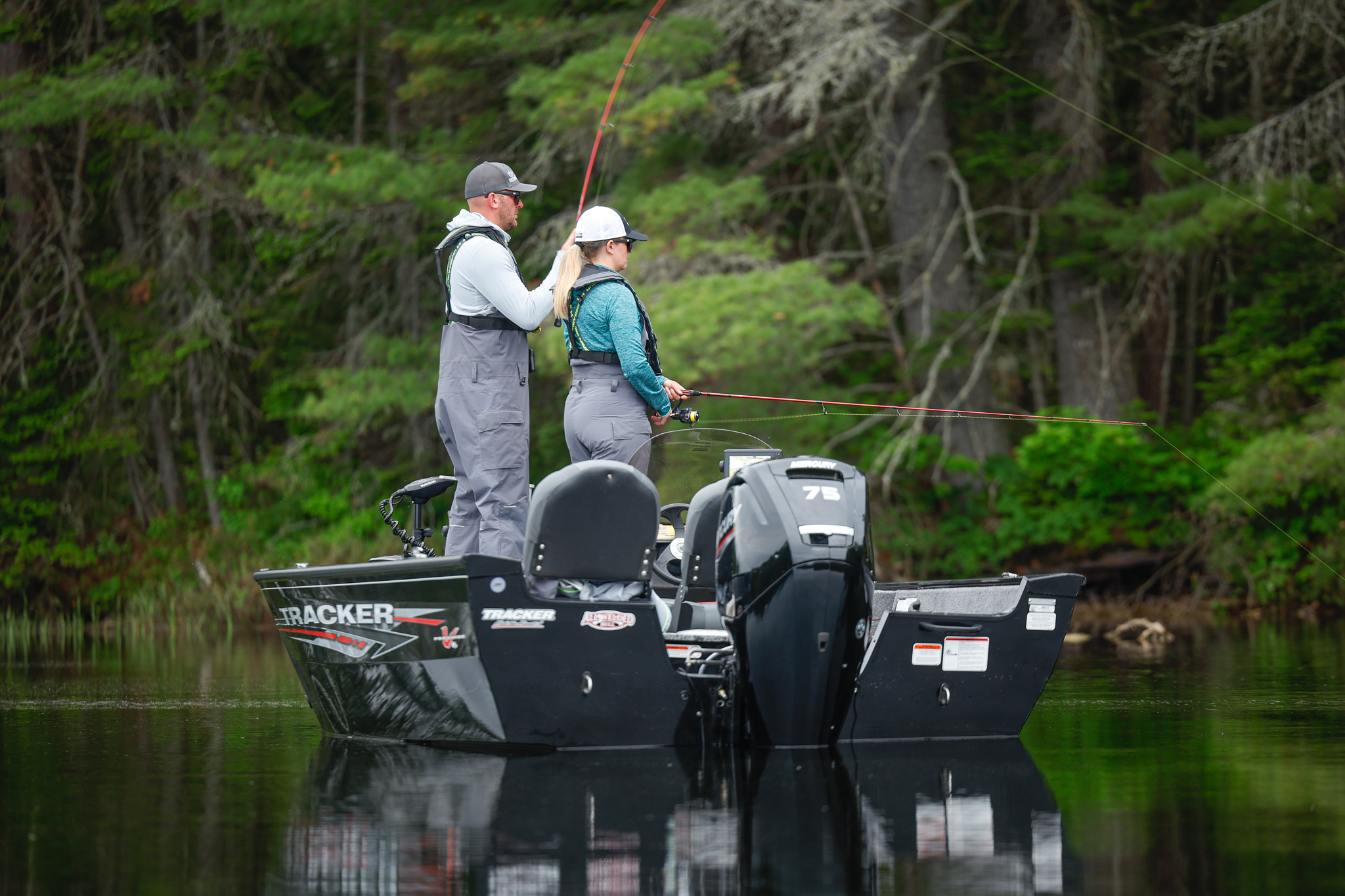 A woman and man with fishing lines in the water while on a boat on a lake.