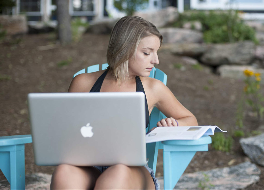 A woman looks a book and laptop, get a California Boater Education card concept.