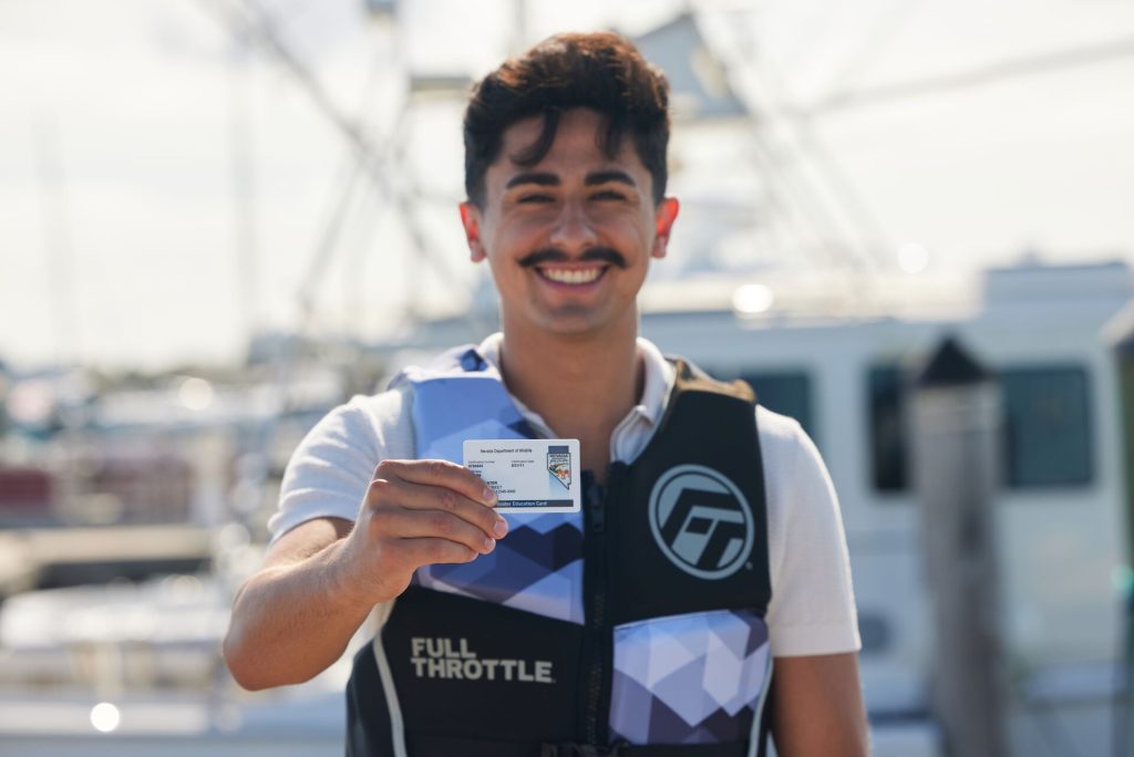 A smiling man in a life jacket with a boater education card.