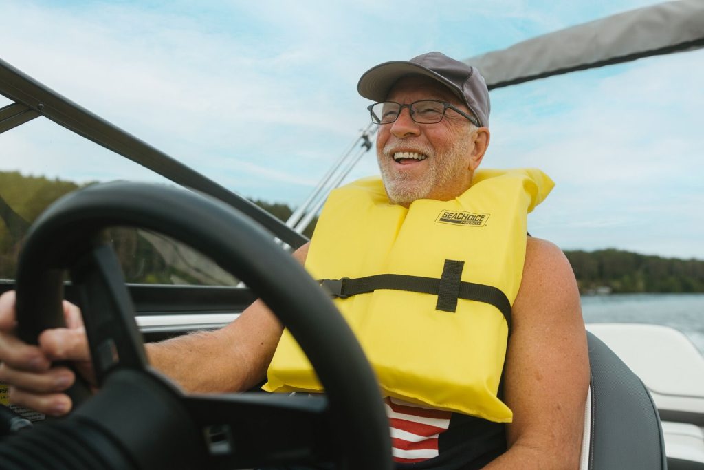 A smiling man in a yellow life jacket drives a boat, good boat servicing for safety concept.