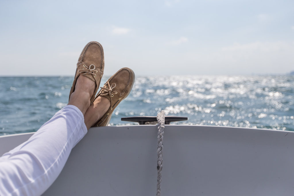 Two feet on propped up on the edge of a boat overlooking the water, boating during coronavirus concept. 