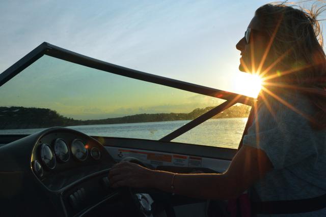 A woman drives a boat at dusk, get a California Boater Card concept.