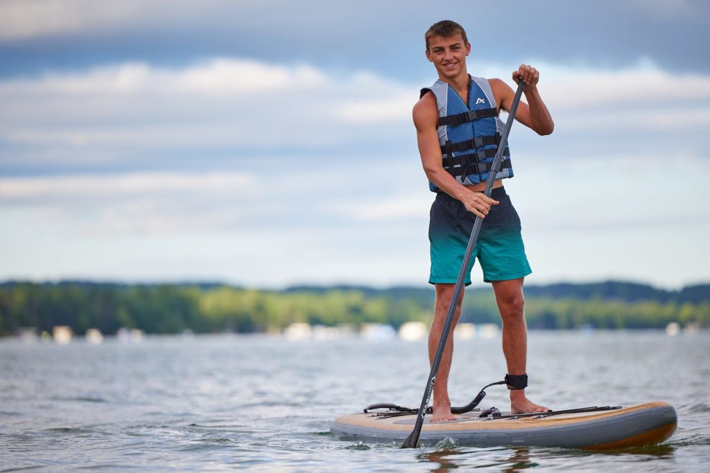 A guy smiling on a paddleboard while wearing a life jacket.