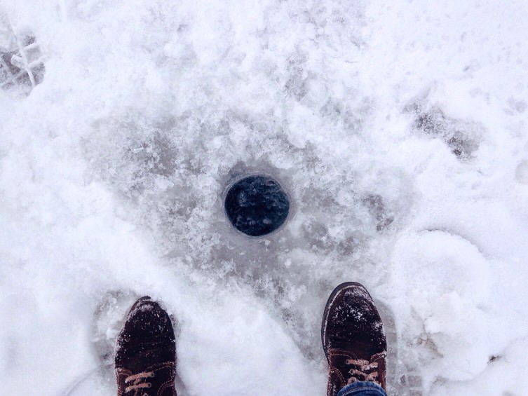 Two feet standing near a hole in the ice, dangers of the spring thaw concept.
