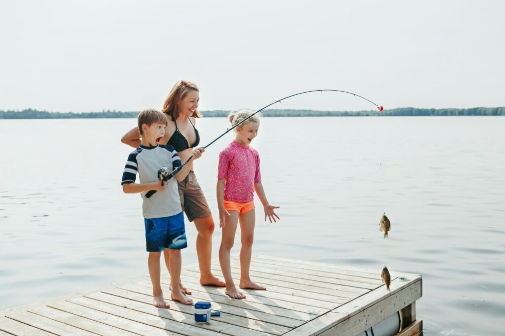 Two kids and a woman catch fish from a dock.