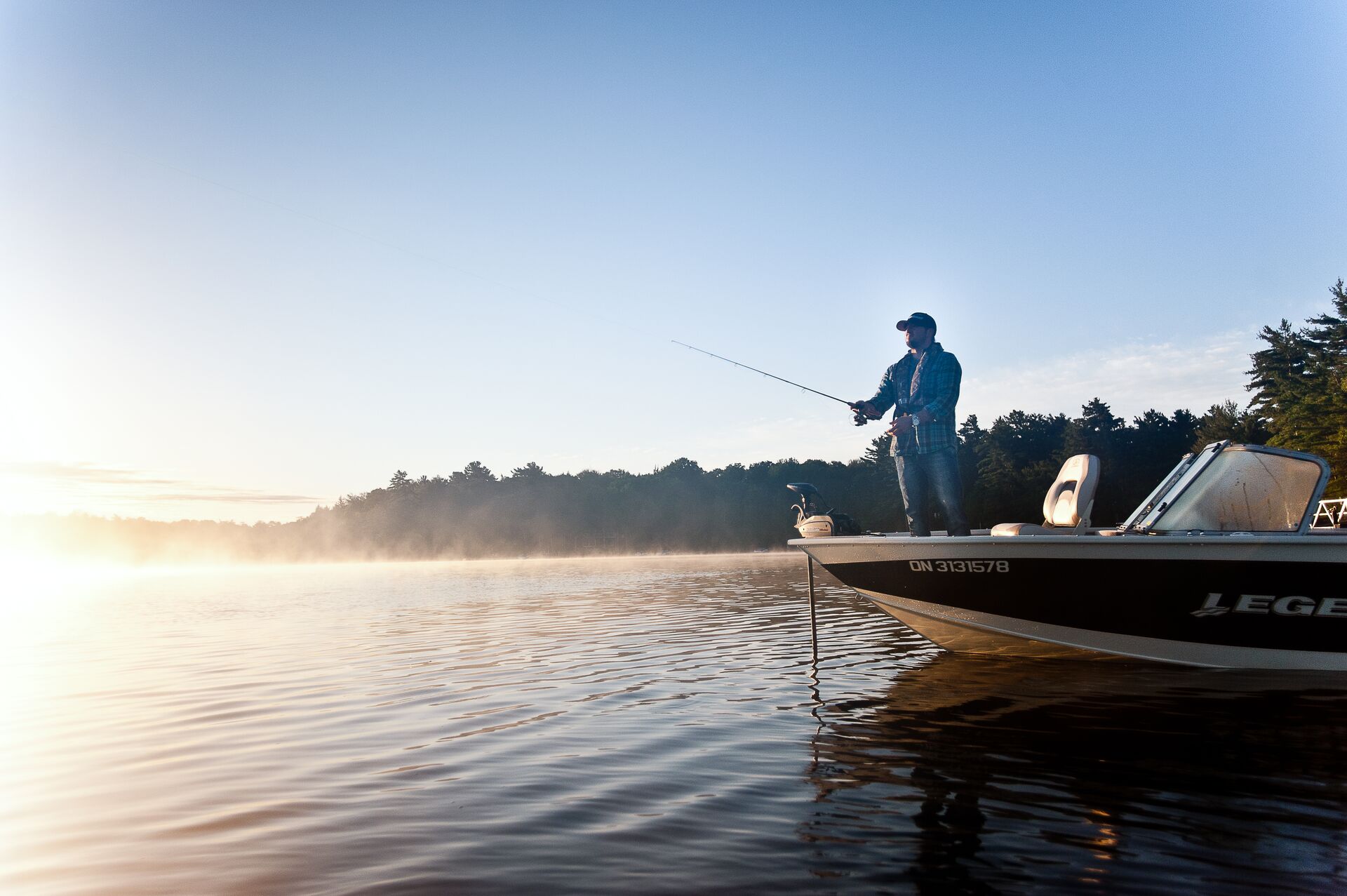 A man at the front of a boat with a fishing line in the water, fishing and boating in New Brunswick concept.