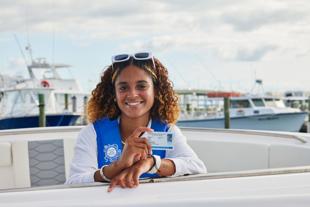 A smiling woman on a boat holds a boater education card, California boater card concept.