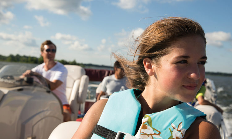 girl sitting in boat with lifejacket on and father in background